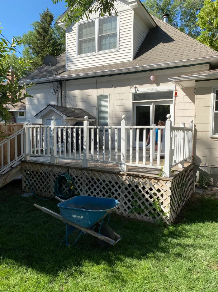 A backyard lawn and a white-railed deck, with a wheelbarrow on the grass.