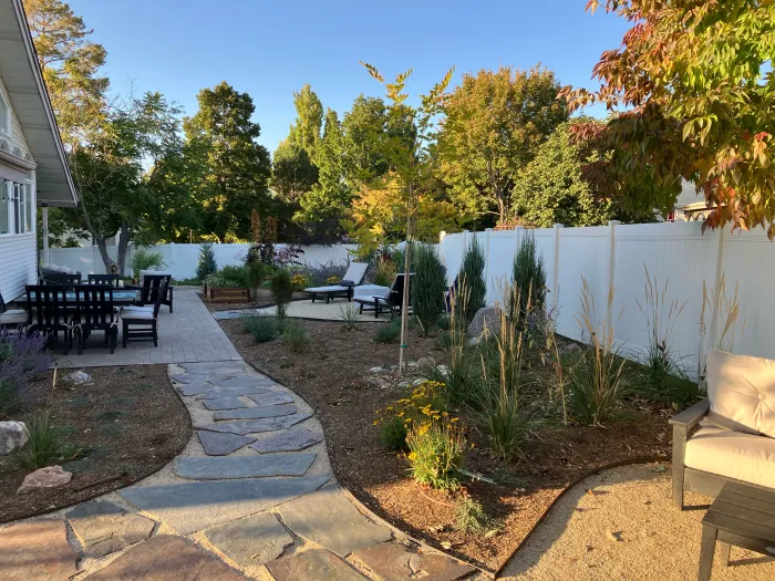 Winding flagstone path through ornamental grasses and perennials beside a patio with an outdoor dining set.
