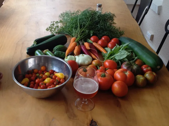 A table of garden vegetables: tomatoes, zucchini, carrots, herbs and a bowl of cherry tomatoes.