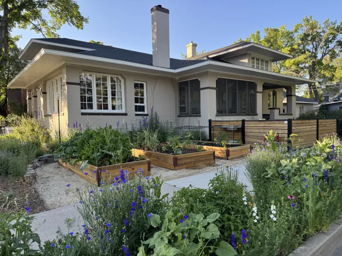 A craftsman bungalow with raised wooden garden beds, flowers and a low fence in the front yard.
